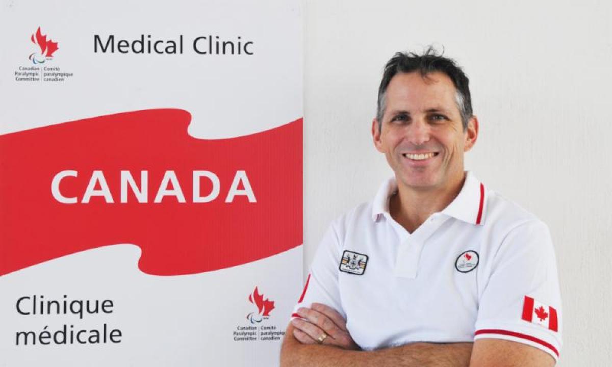 man looking at the camera with arms crossed in front of Canadian banner