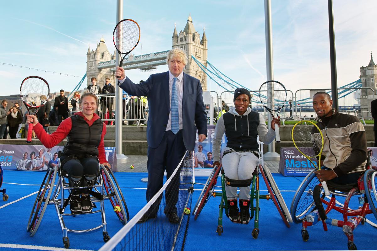 three wheelchair tennis players and the Mayor of London holding tennis rackets up in front of London Bridge