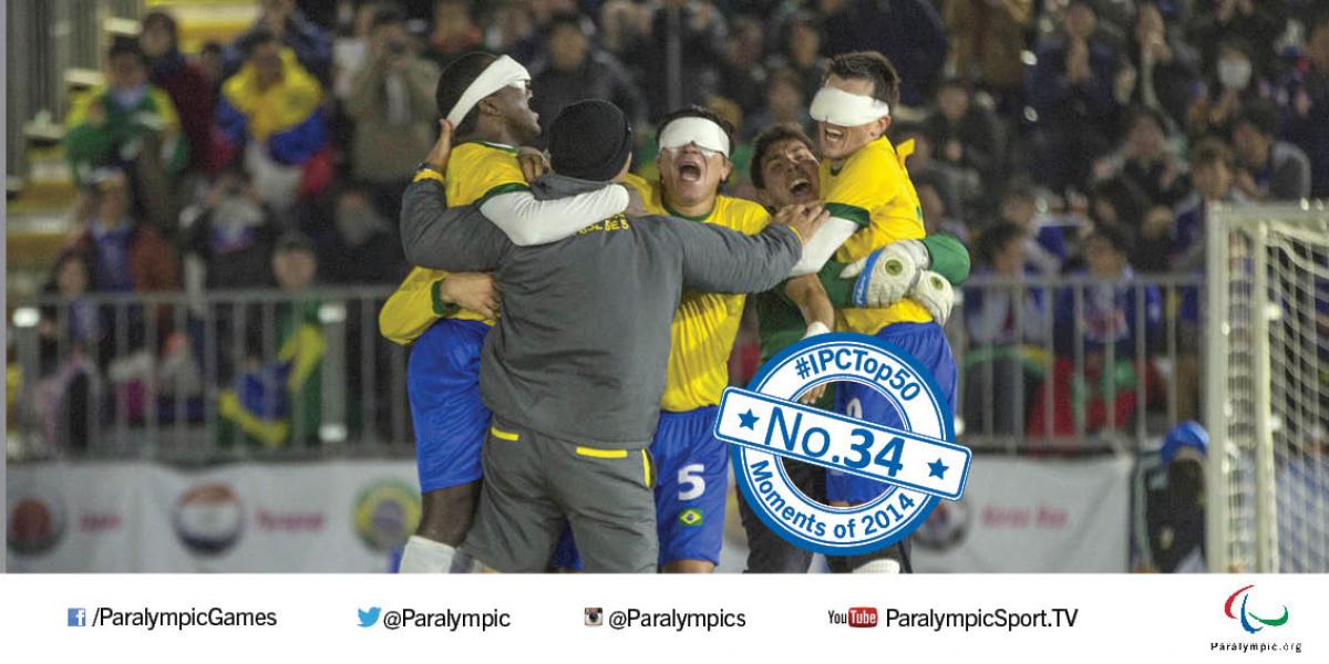 A group of five men, three blindfolded and wearing football shirts, jump up and hug in celebration