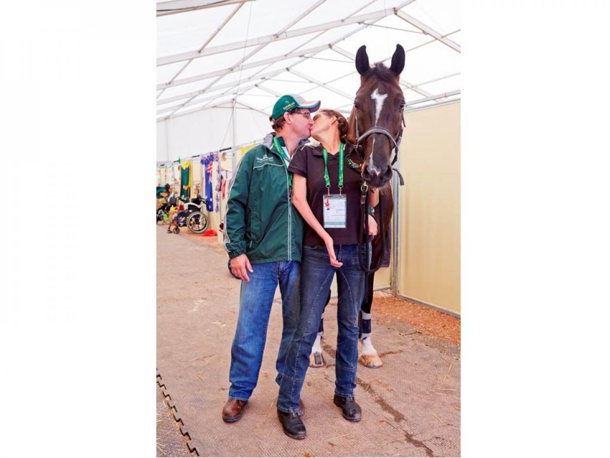 Man and women kissing, a black horse stands next to them.