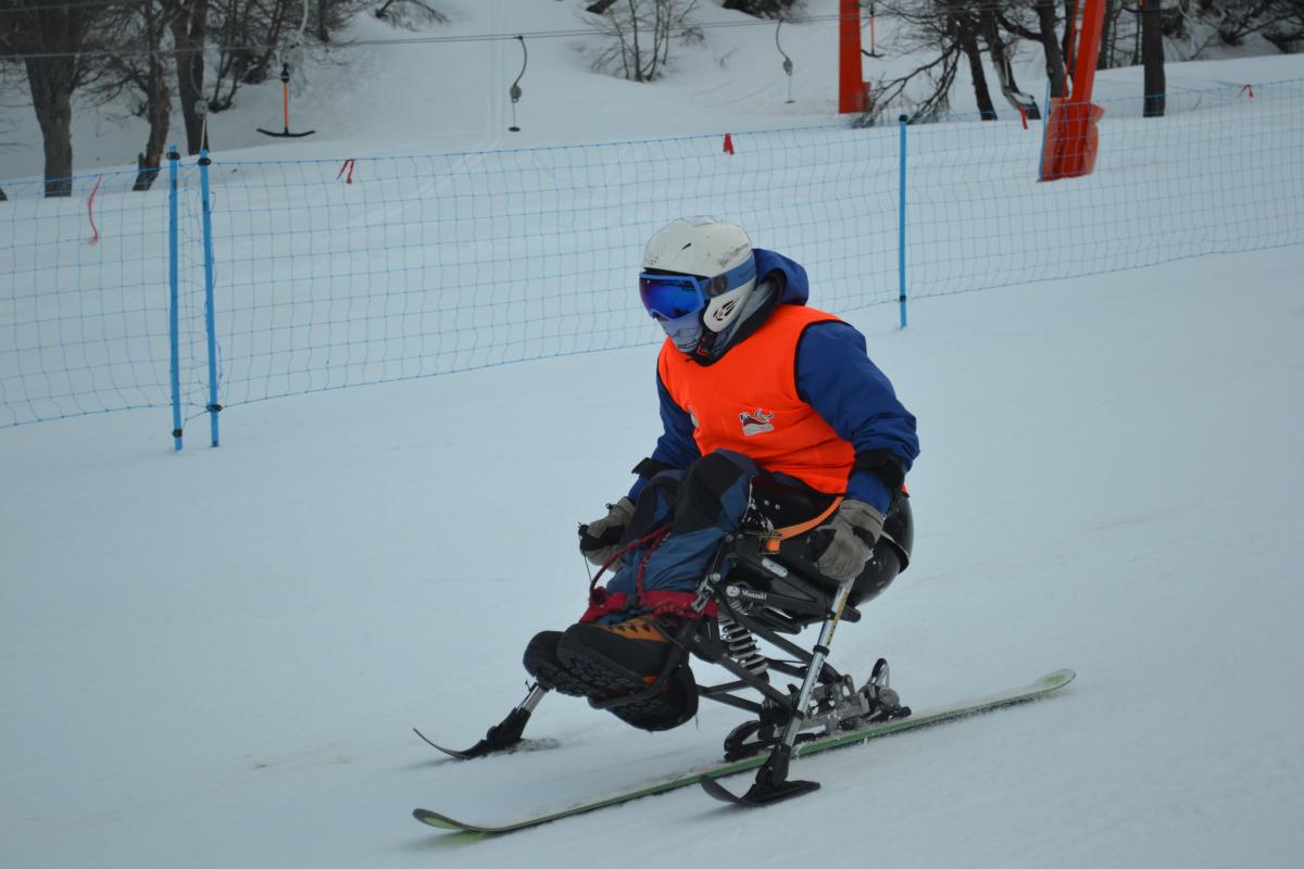 Child in a sit ski skiing down a slope.