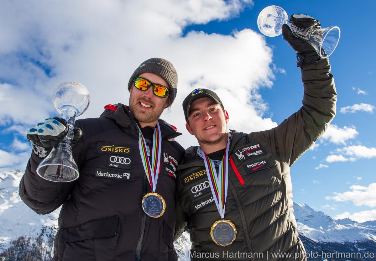 Upper bordies of two men smiling, showing their medals to the camera