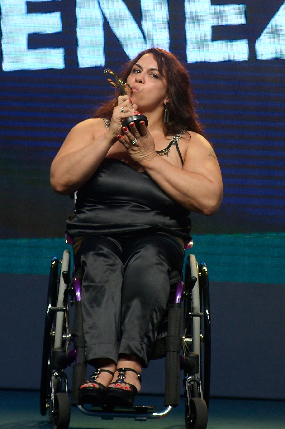 Women in black dress sitting in a wheelchair kissing a trophy