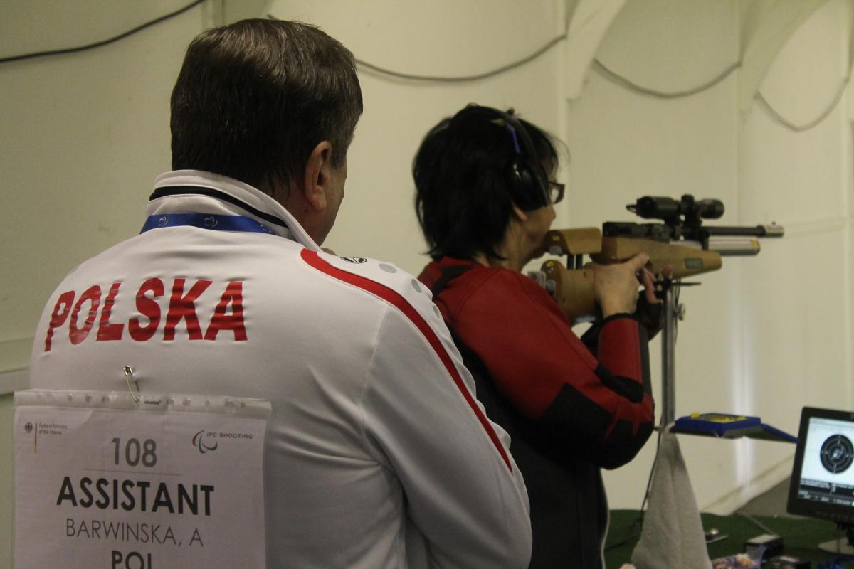 Women in a shooting range with a man standing behind her