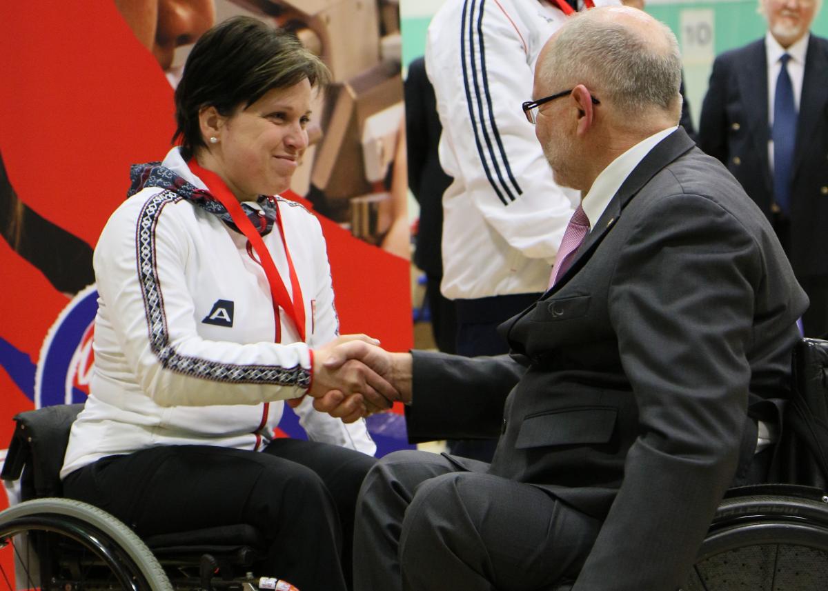 A female shooter in congratulated by a medal presenter