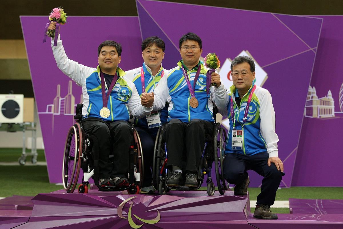Four athletes in a wheelchair on a podium celebrating their medals.
