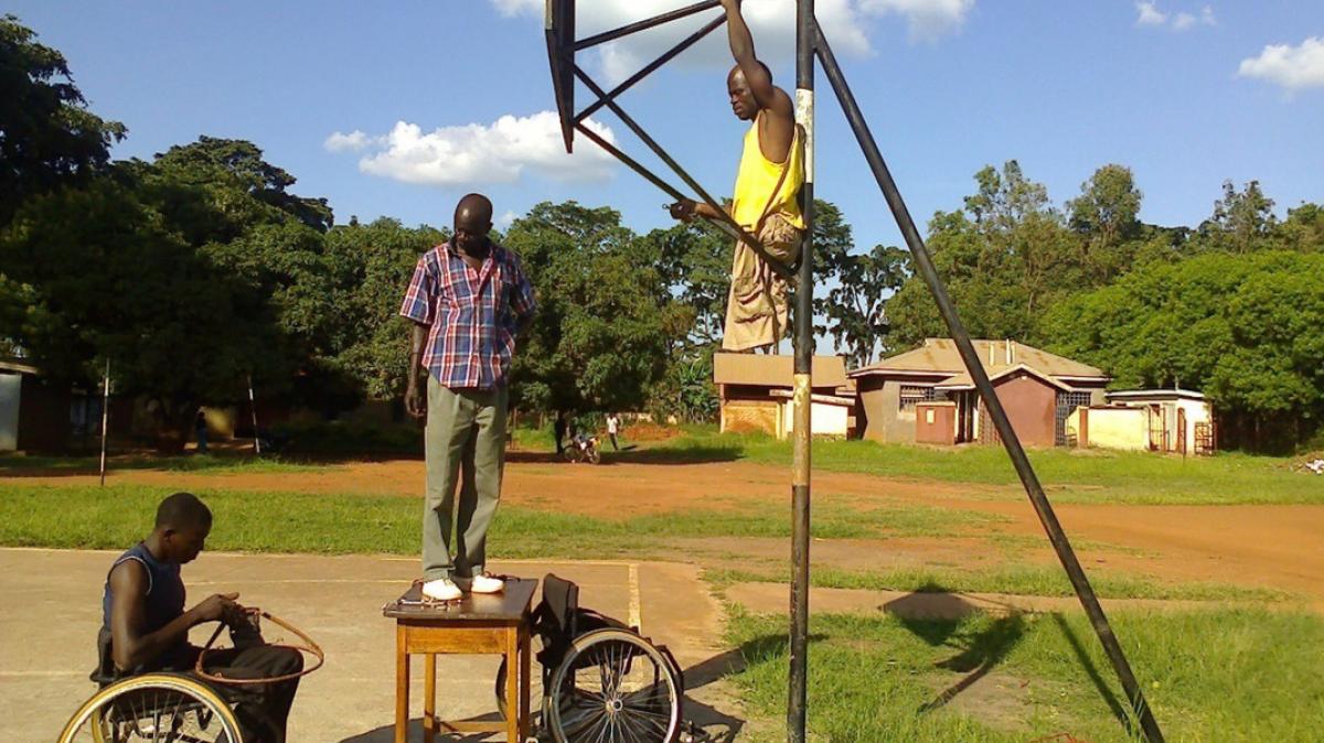 Three Ugandan men prepare the court for wheelchair basketball