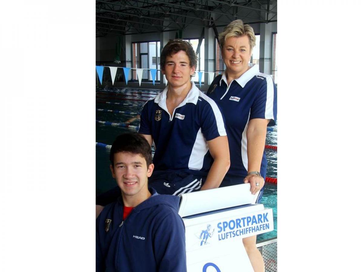 Two young boys and an adult woman pose in front of a swimming pool