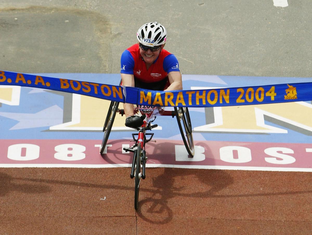 Women in racing wheelchair crosses a finish line