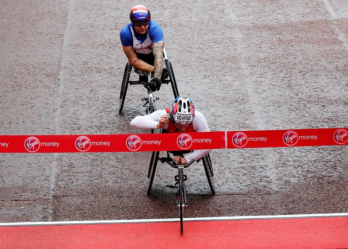 A wheelchair racer cuts through the finishing tape on a wet damp road.