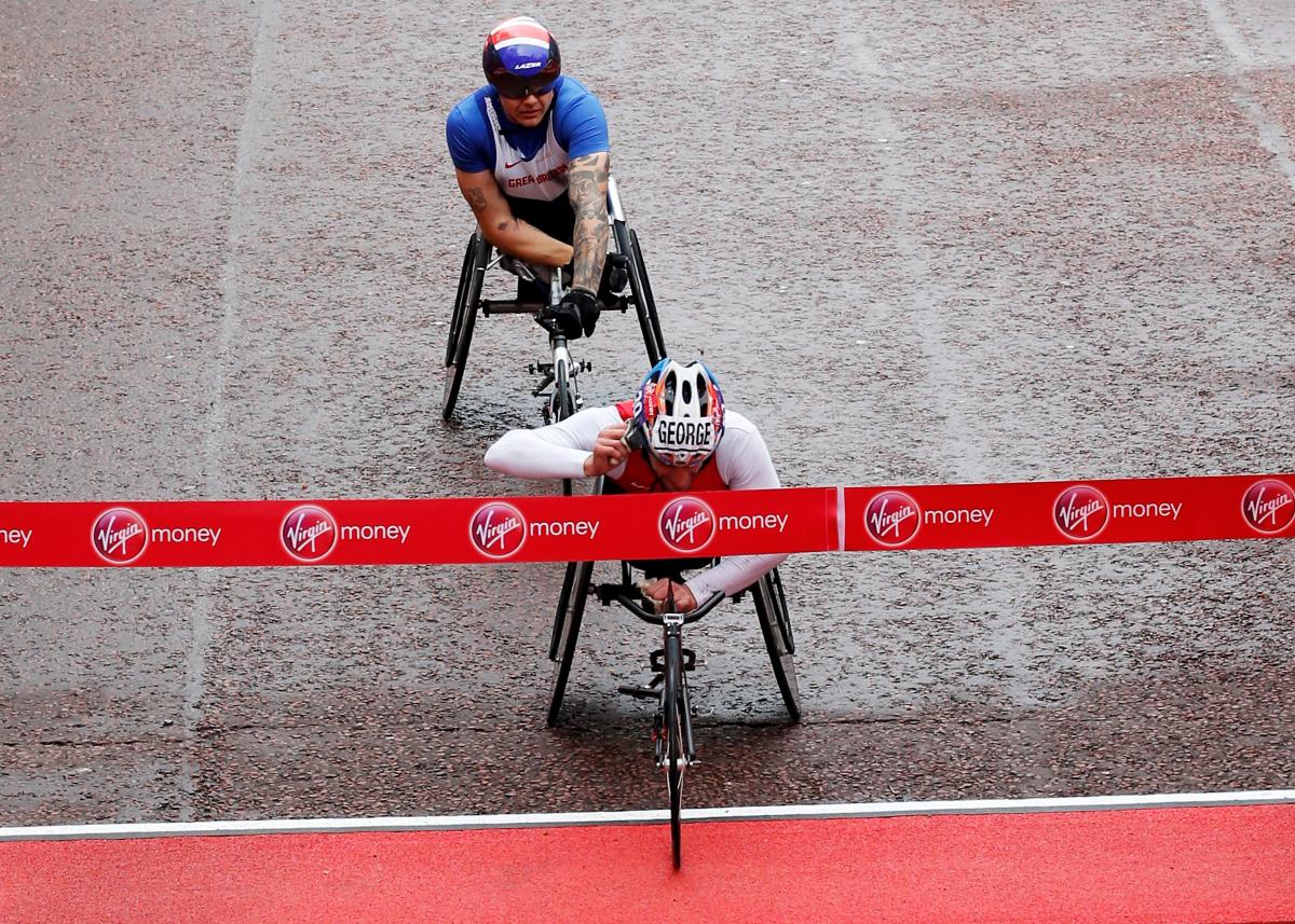 Josh George London Marathon A wheelchair racer cuts through the finishing tape on a wet damp road.
