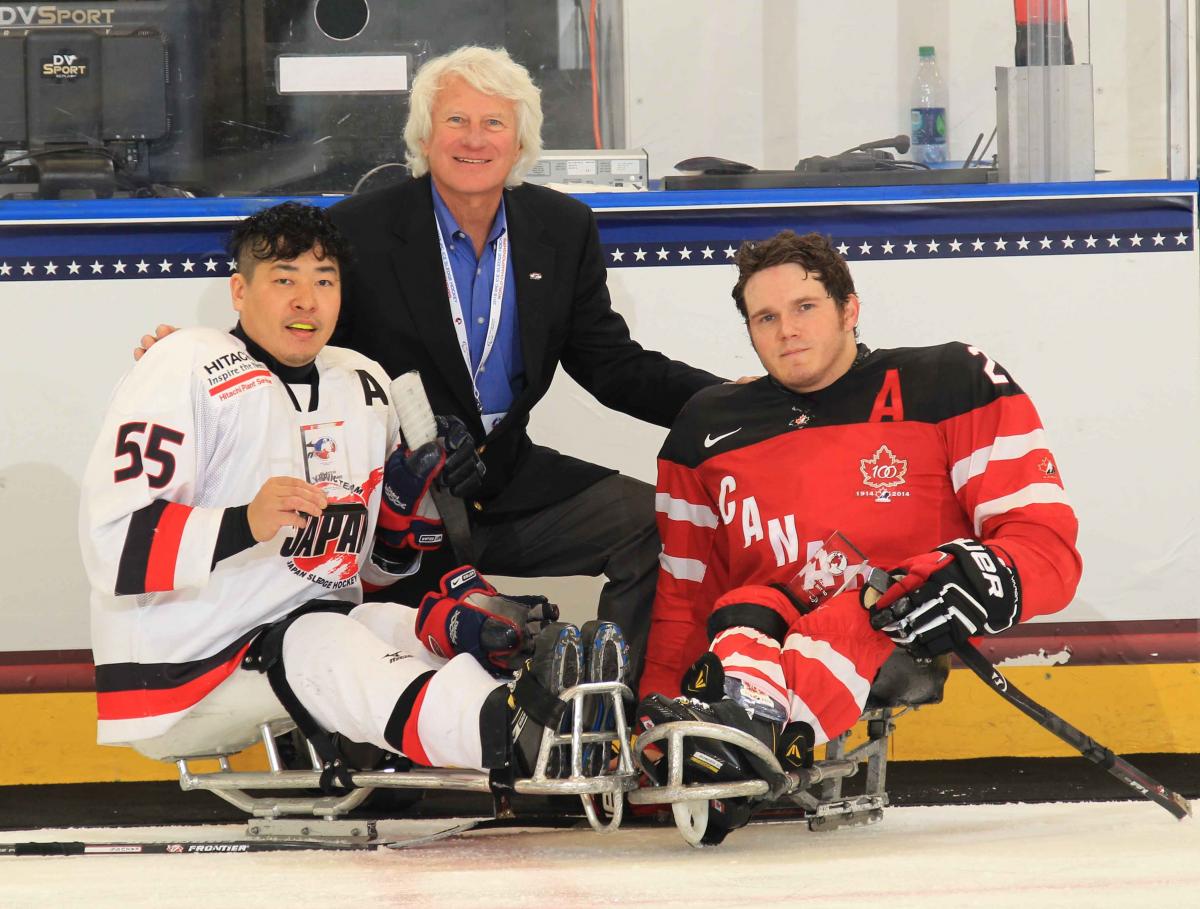 Two sledge hockey players and a man in a suit posing for the camera