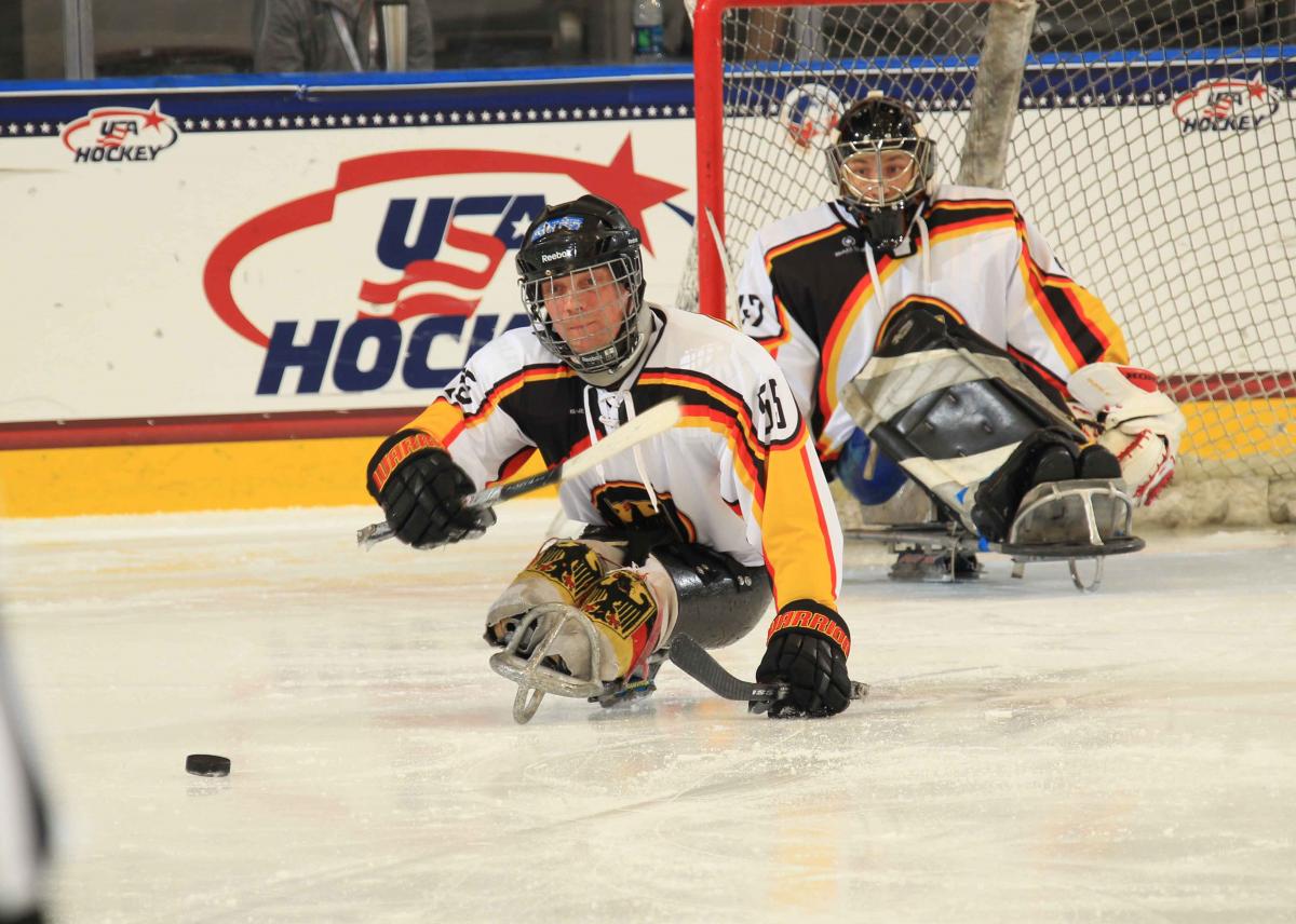 Two players on sledges on the ice, one focusing the puk