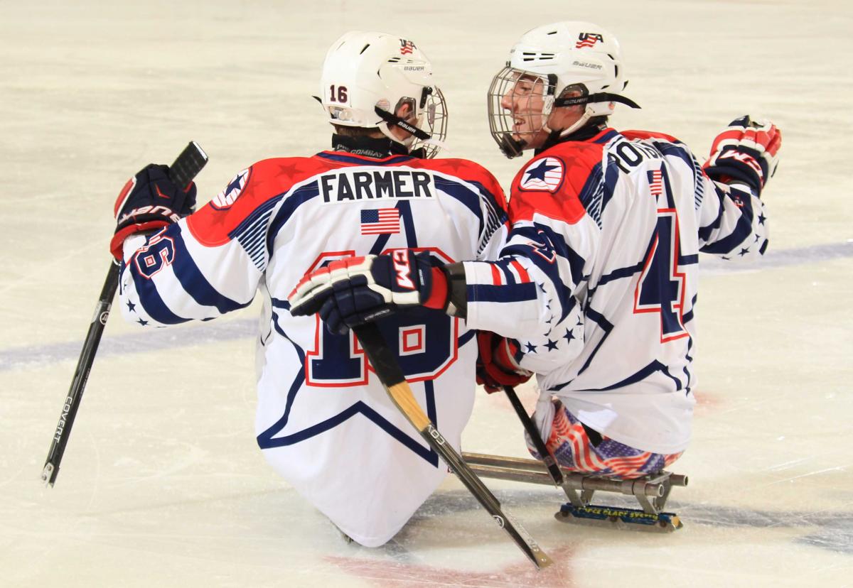 Two sledge hockey players on the ice, in a conversation