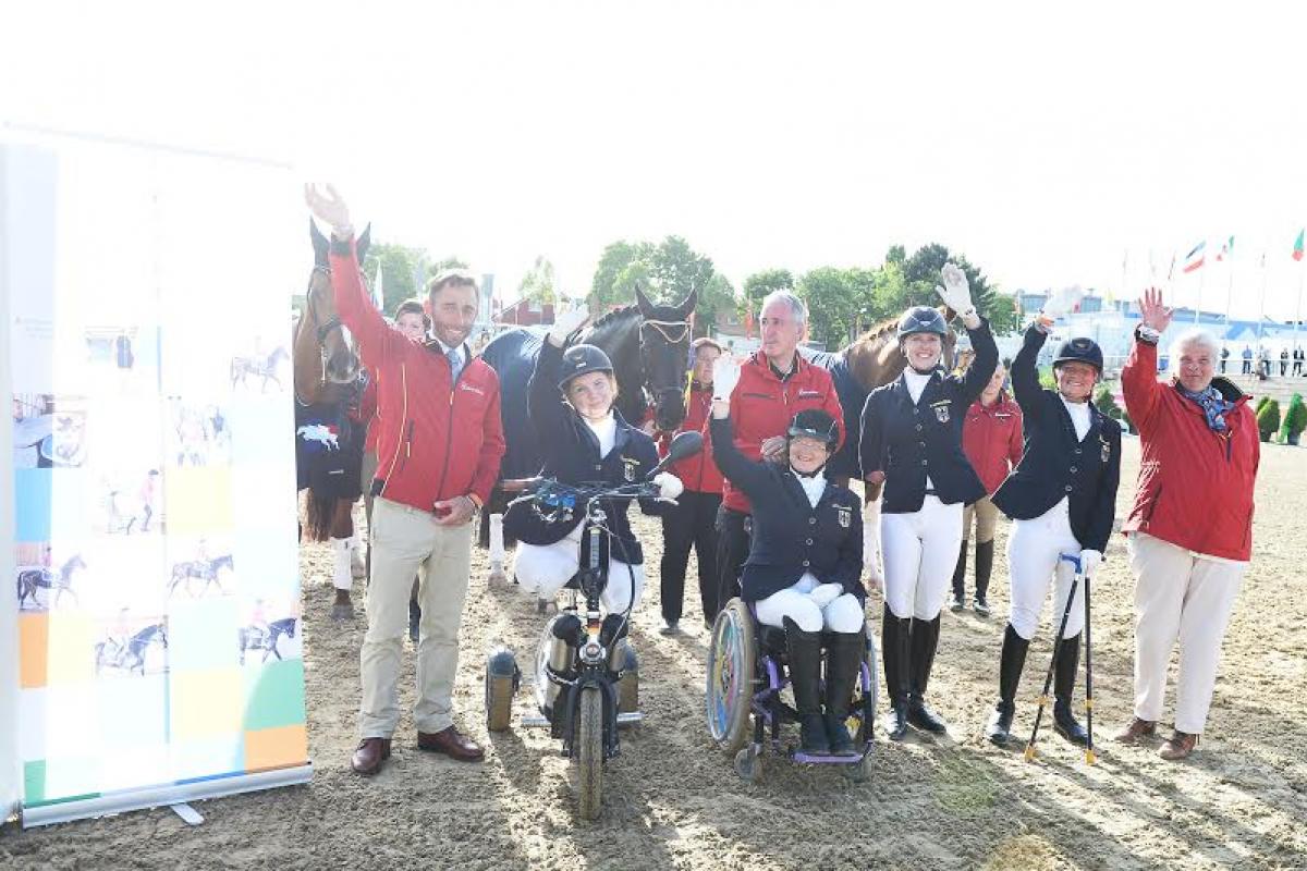 Group shot of seven people and horses in the background, waving to the camera