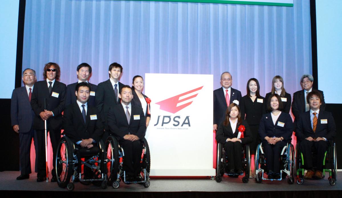 Group shot of around 20 people standing and in wheelchairs with a big banner