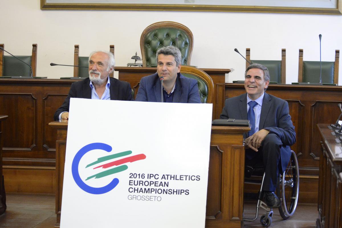 Three men behind a table present the logo for the 2016 IPC Athletics European Championships.