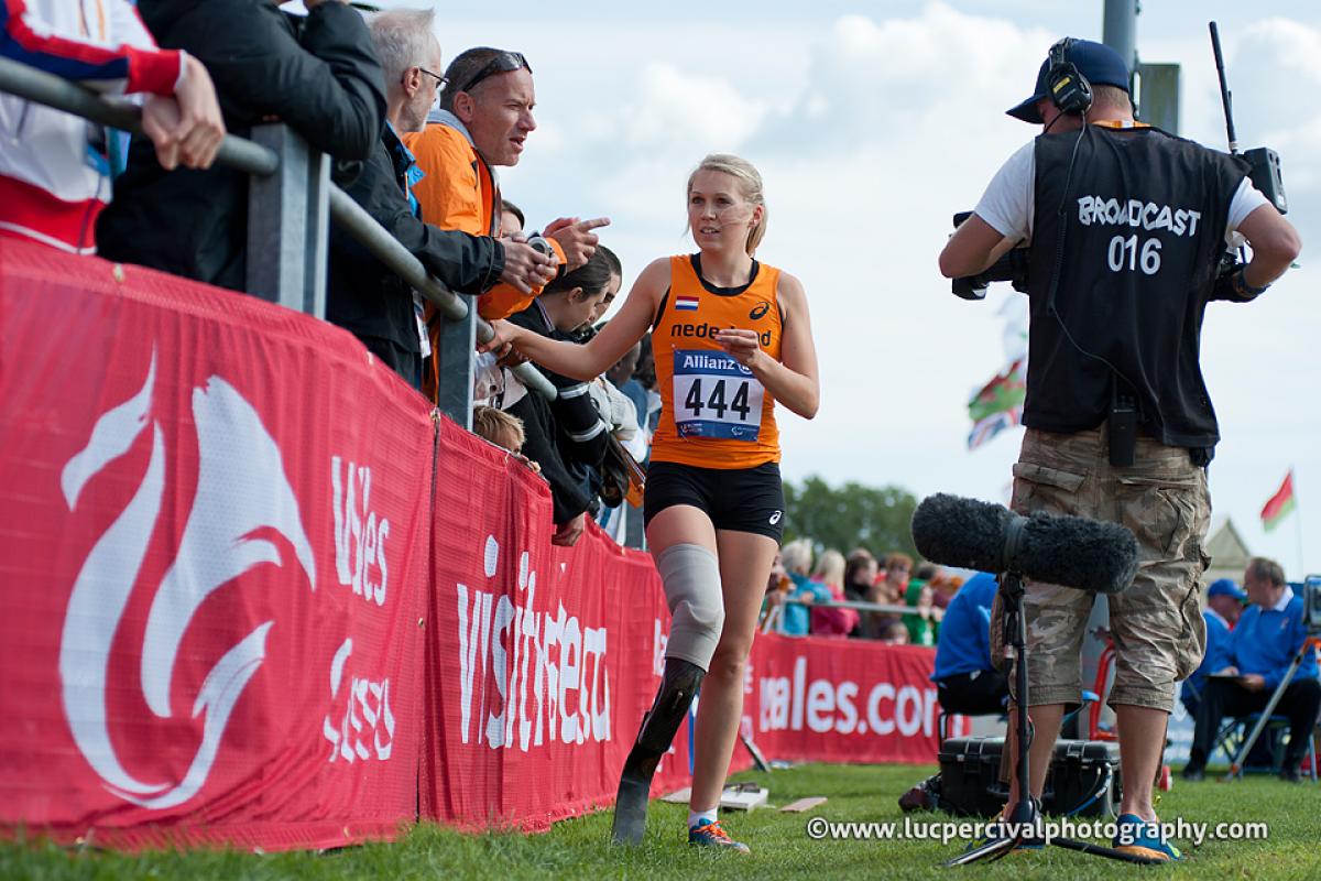 women in jersey with prosthetic leg speaking to a man in orange jersey, both filmed by a camera