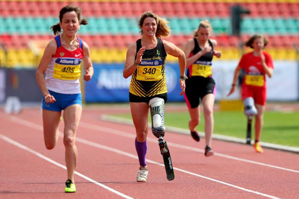 A woman with a running blade clenches her face in effort as she sprints forward.