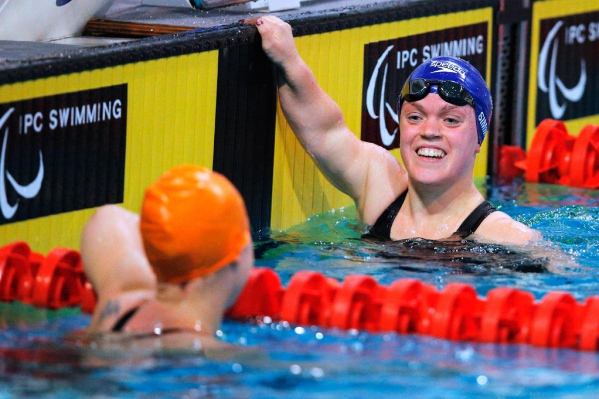 Two women smiling at each other in a swimmig pool after a race