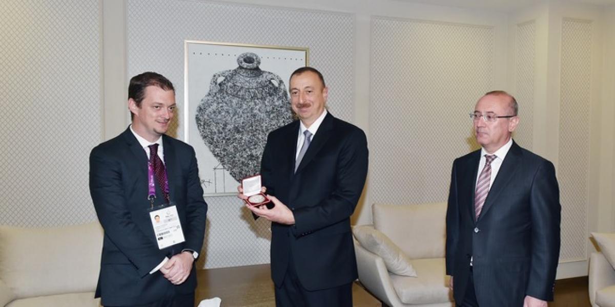 Three men in suits, one of them showing an award to the camera.