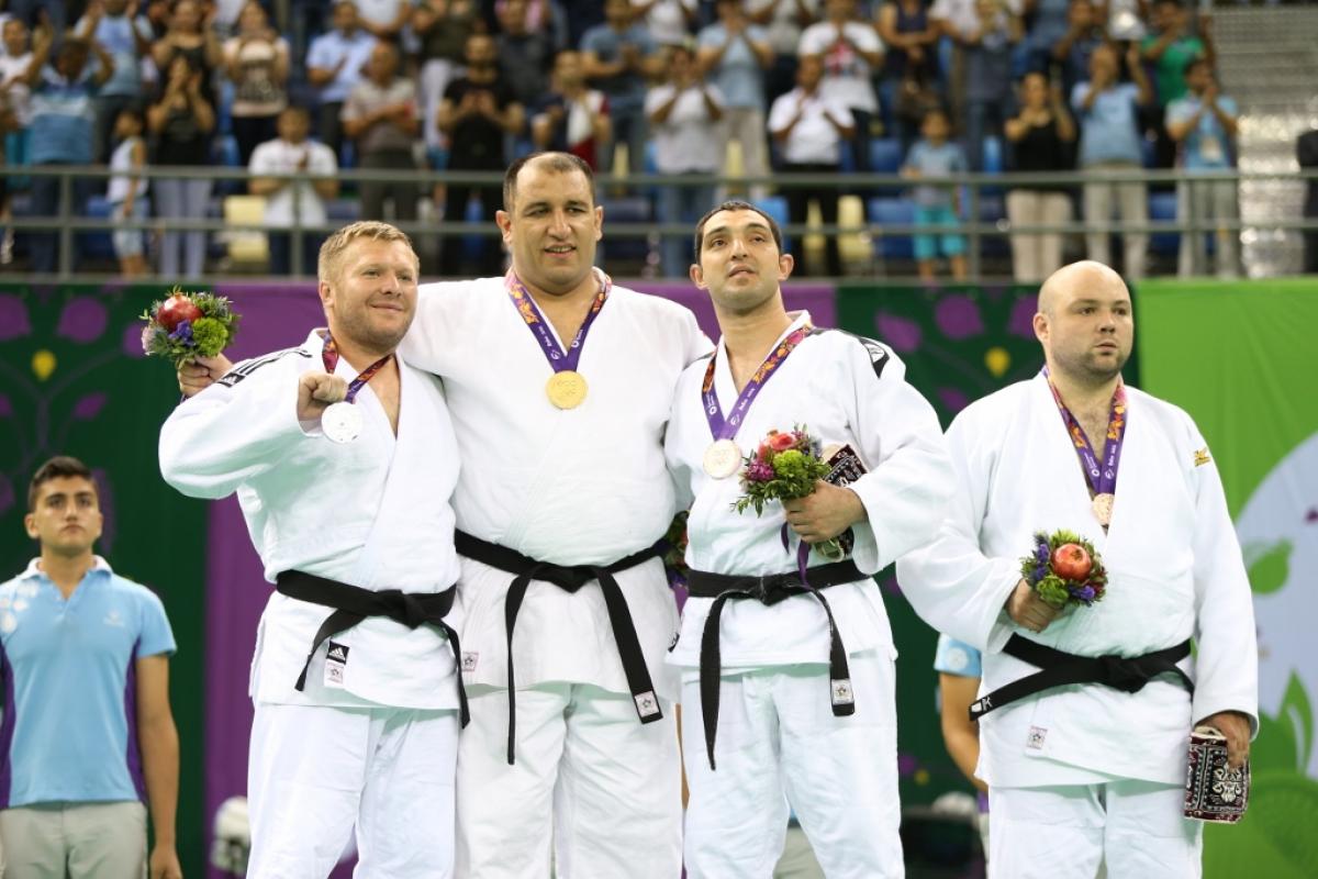 Four male judoka pose on podium