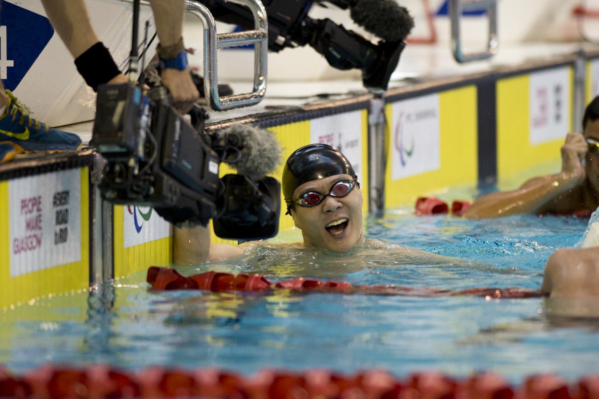 Man in swimming pool, celebrating after finishing a race. Camera filming him.