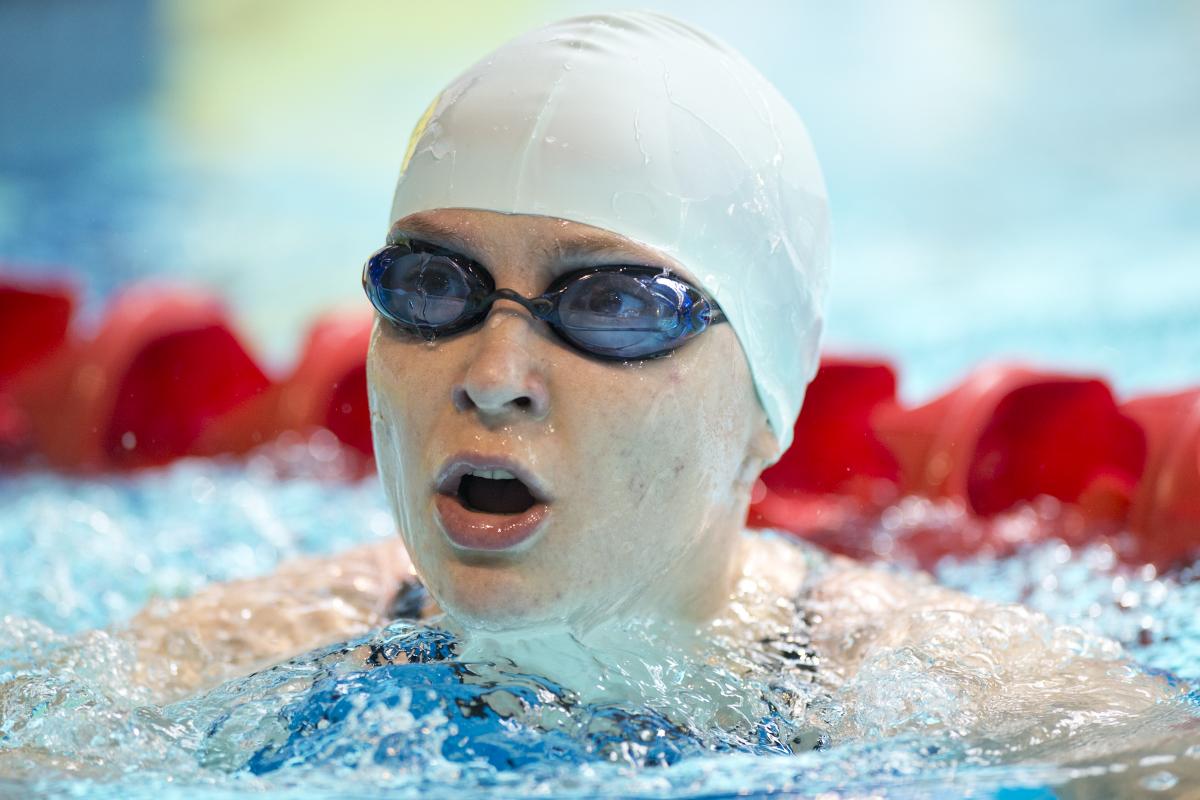 Portrait picture of a swimmer with a white swim cap and swim goggles.