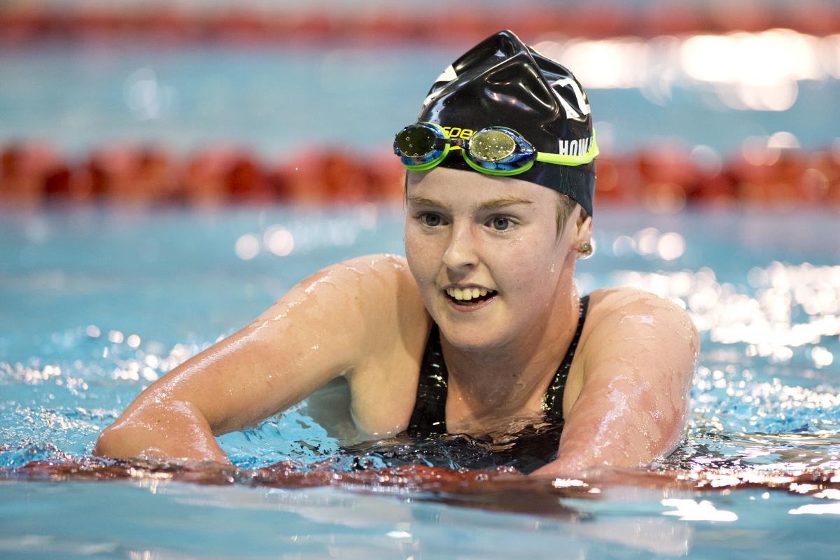 Woman in swimming pool, upper body is out of the water, smiling