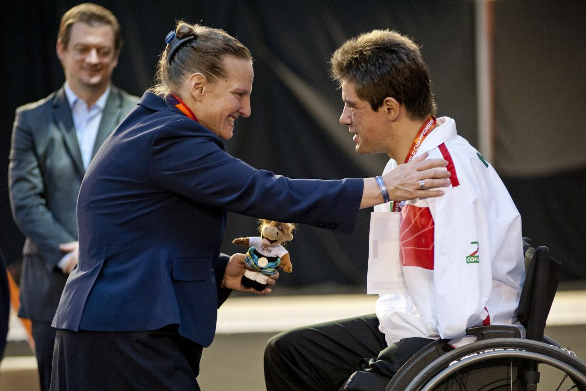 Man in wheelchair on the podium receiving a medal from a woman