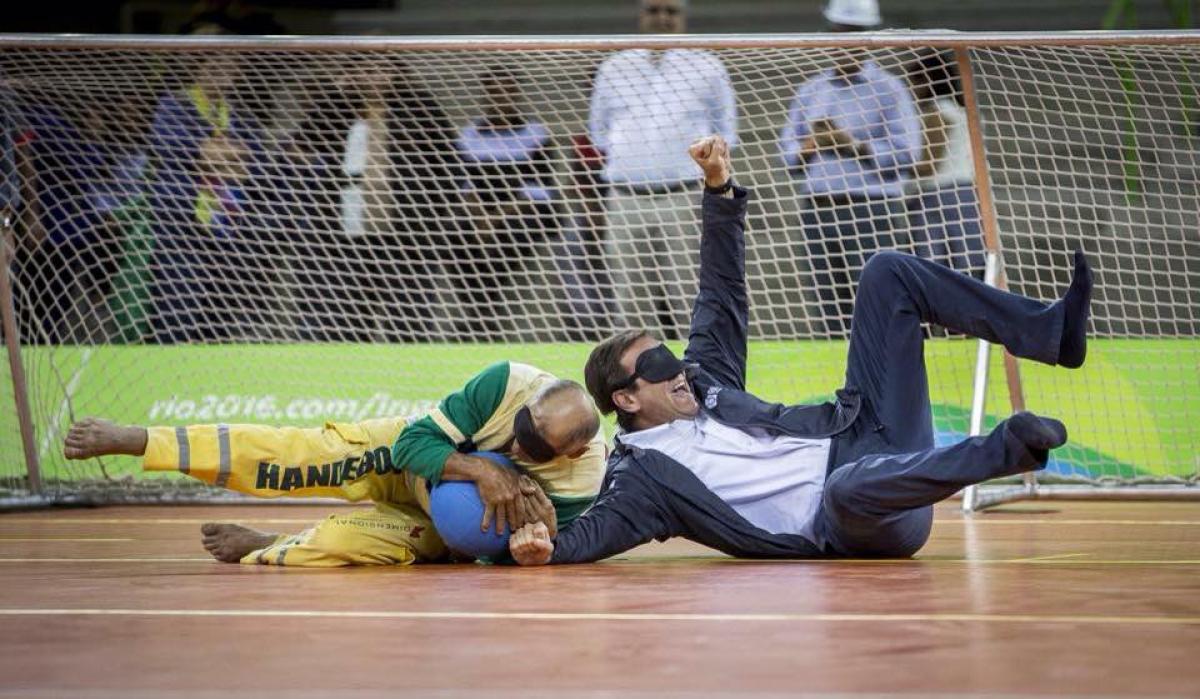 Two blindfolded men, one in a suit lying on a field of play, catching a ball