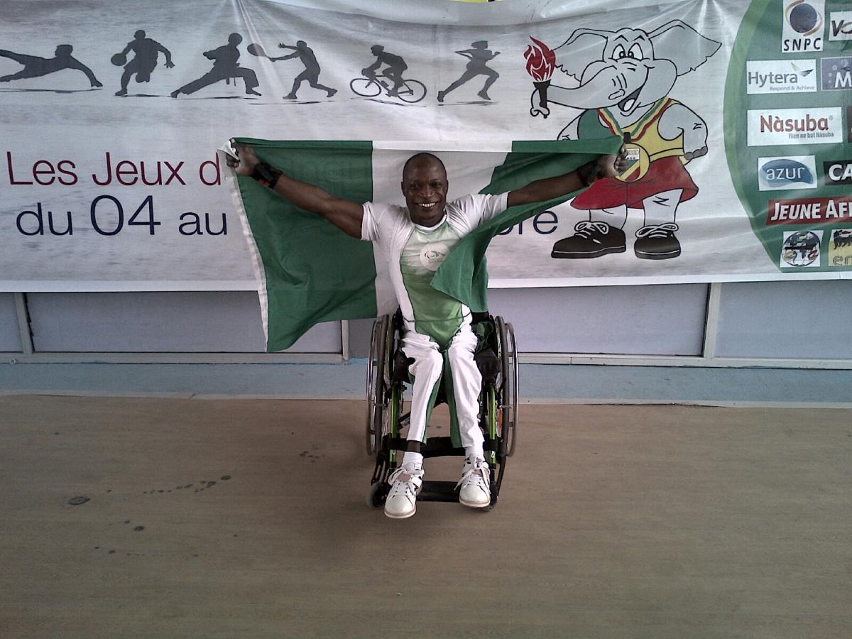 Man in a wheelchair, holding a Nigerian flag and celebrating