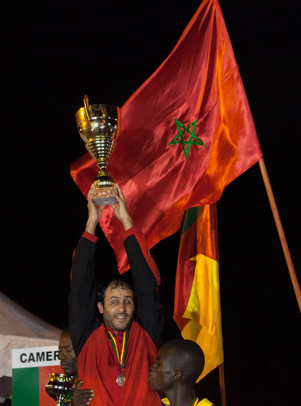 Man celebrates victory by raising football cup.