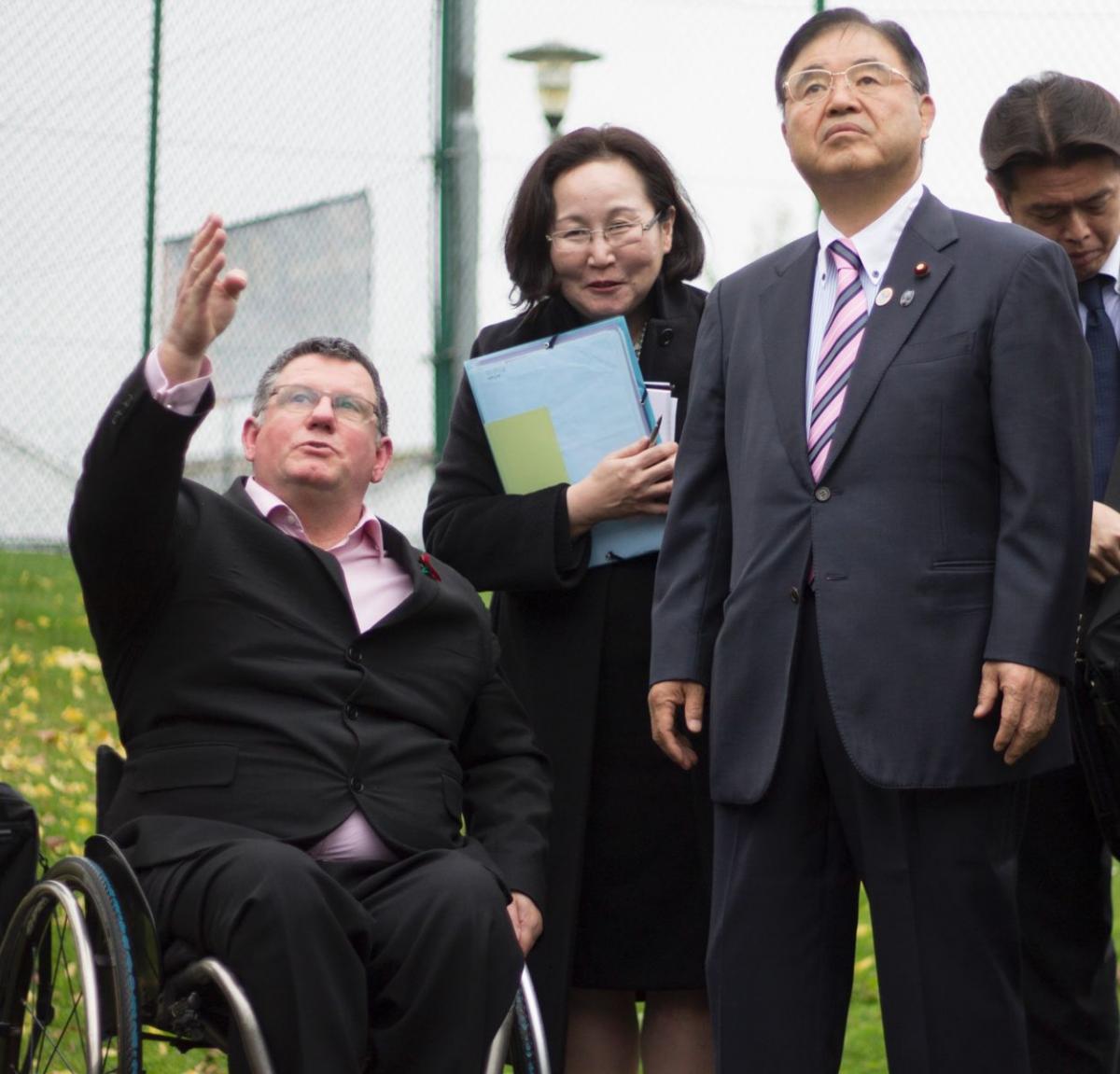 Man in wheelchair points at something, shows something to a man and woman.