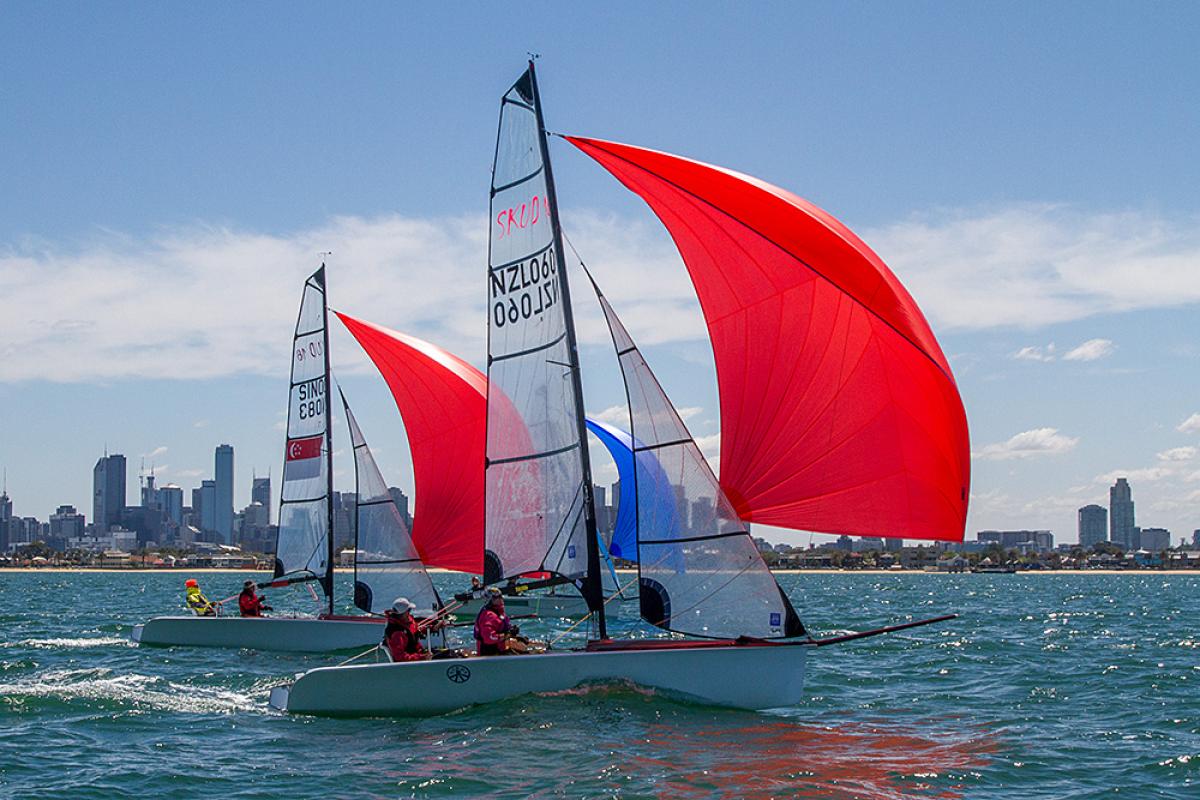 Two boats with red sails on the water in front of a skyline