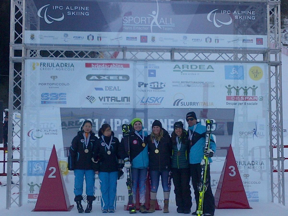 Women's visually impaired slalom podium - 2016 IPC Alpine Skiing World Cup Tarvisio, Italy Podium of six people in front of a branded wall