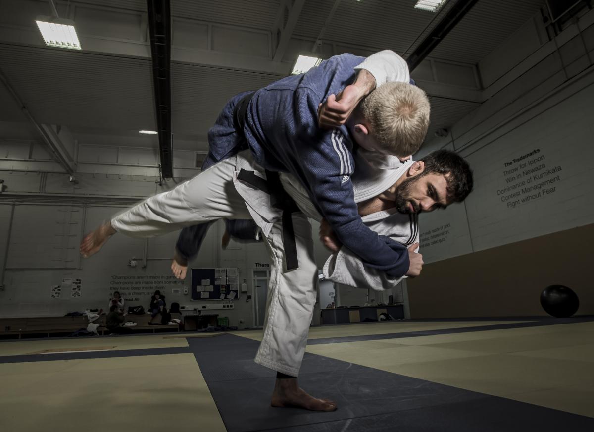 A male judoka in a while suit puts a move on another male judoka in a blue suit. 