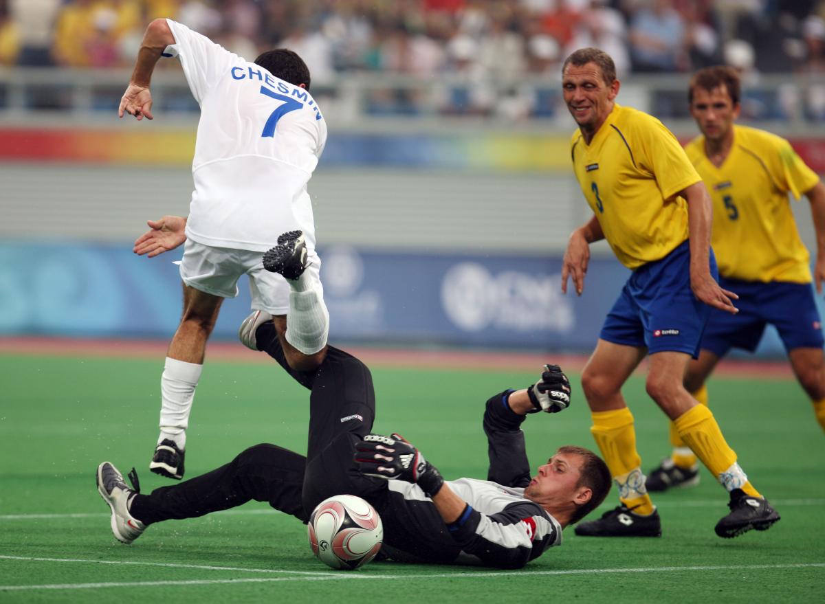 Man on the ground. other man jumping over him. Both focusing on a ball