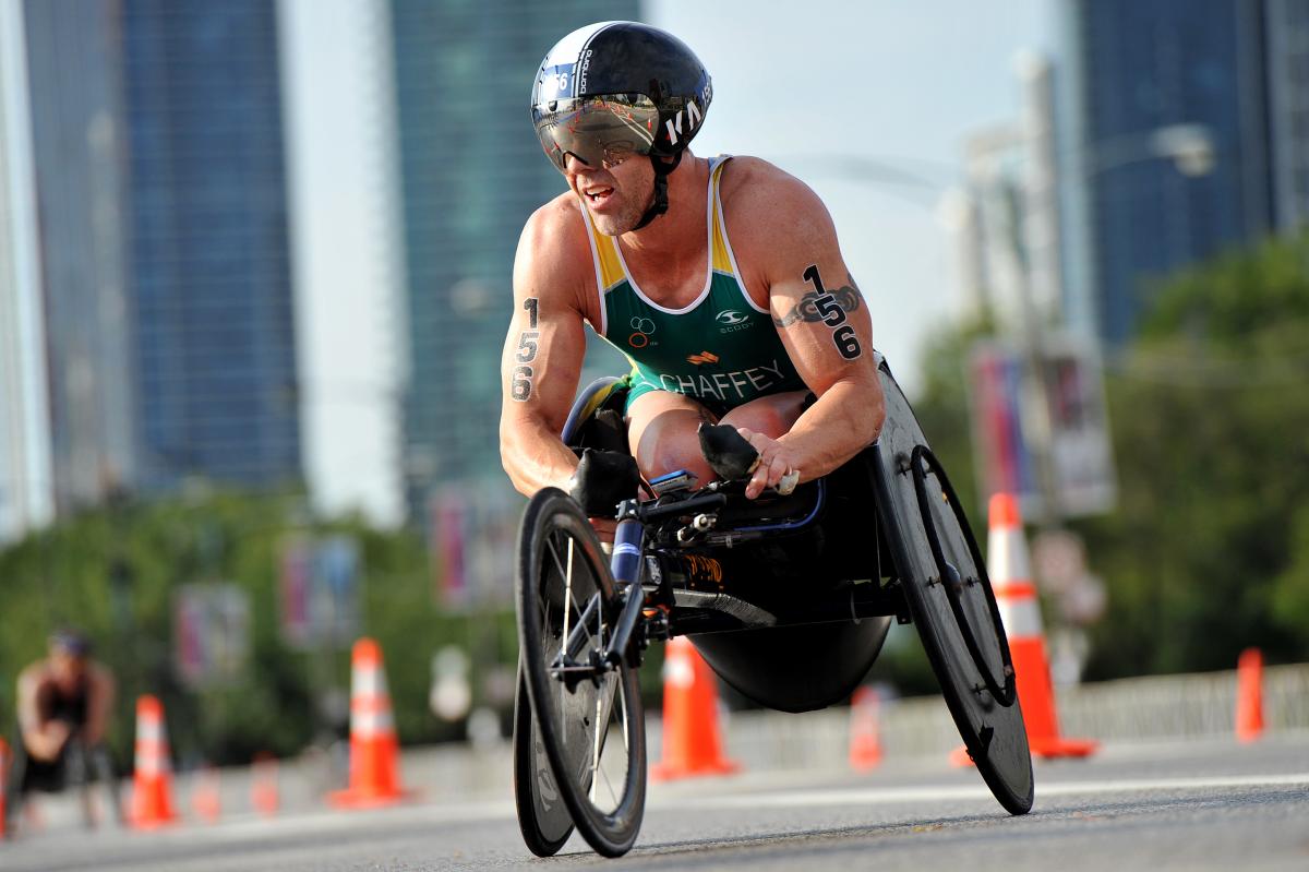 Man in green jersey in a racing wheelchair on a street