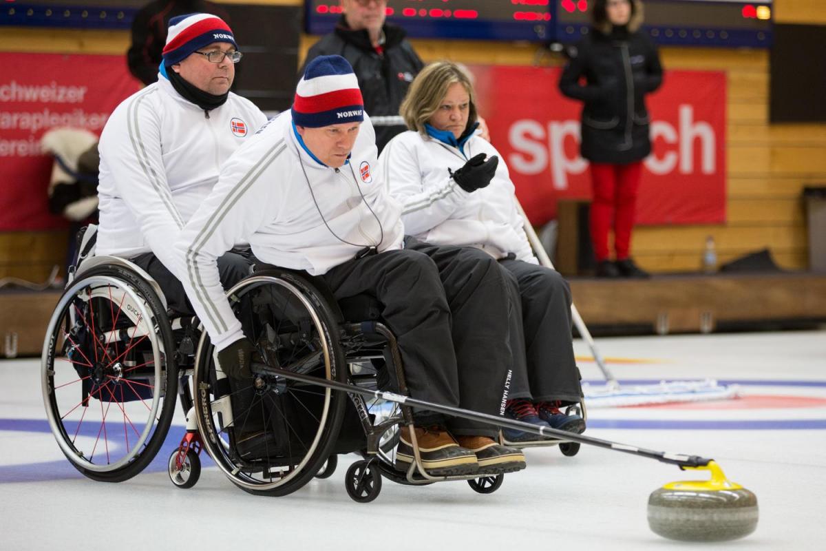 Wheelchair curler on the ice with team in the background