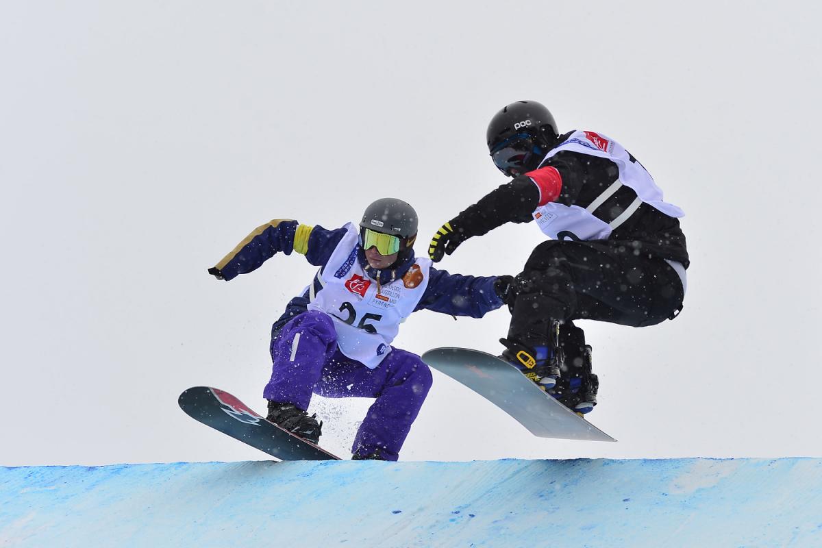 Two snowboarders jumping during a run