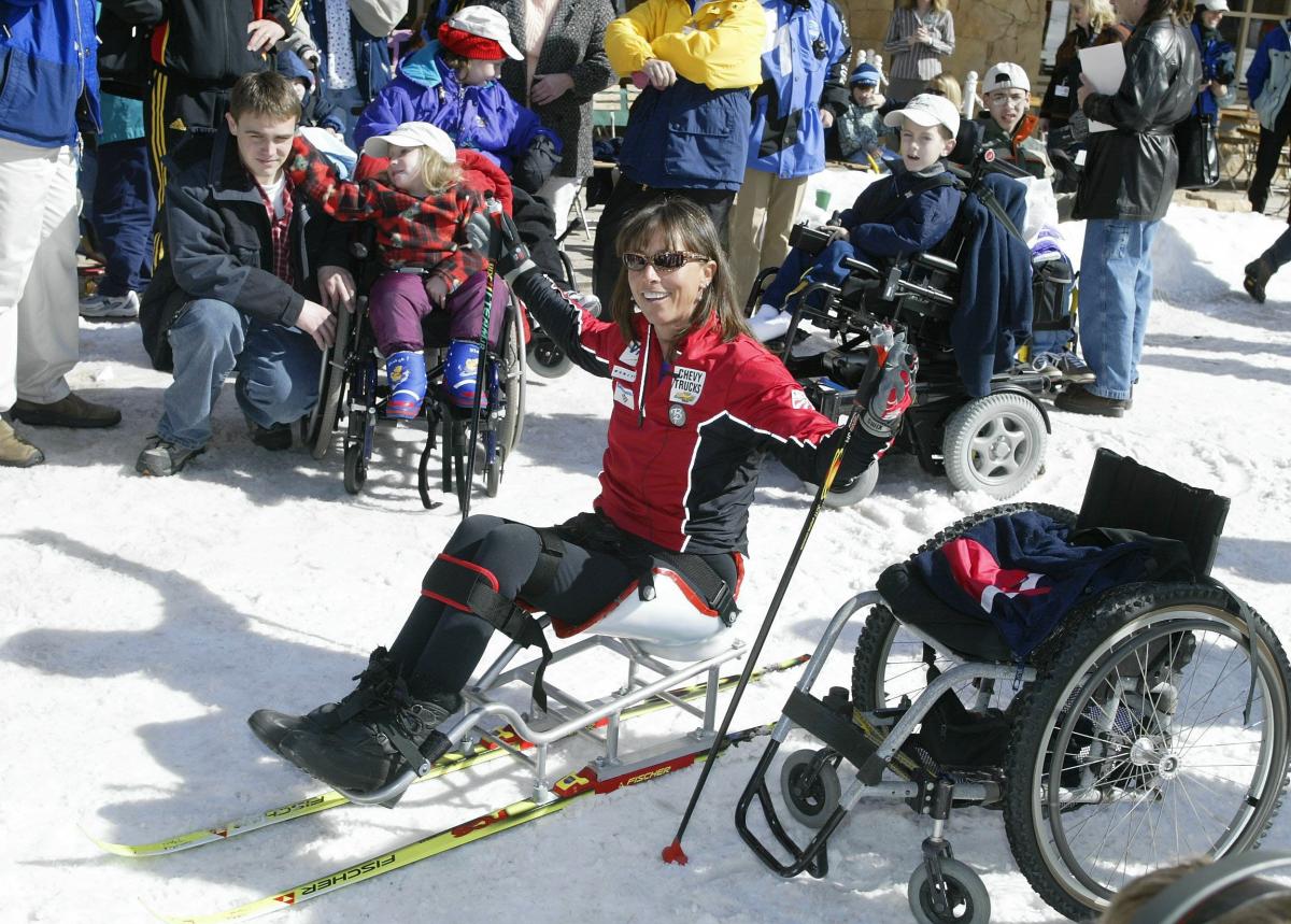 Woman in sit-ski speaks to children. 