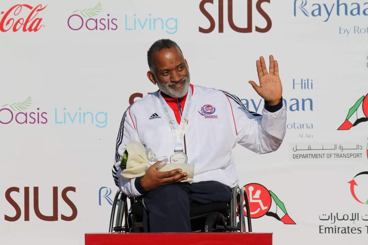 Man in wheelchair holding a medal, waving