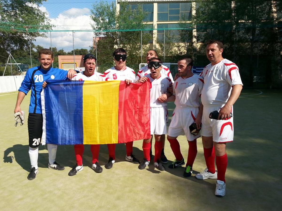 Seven men, some of them blindfolded hold a Romanian flag, celebrate.