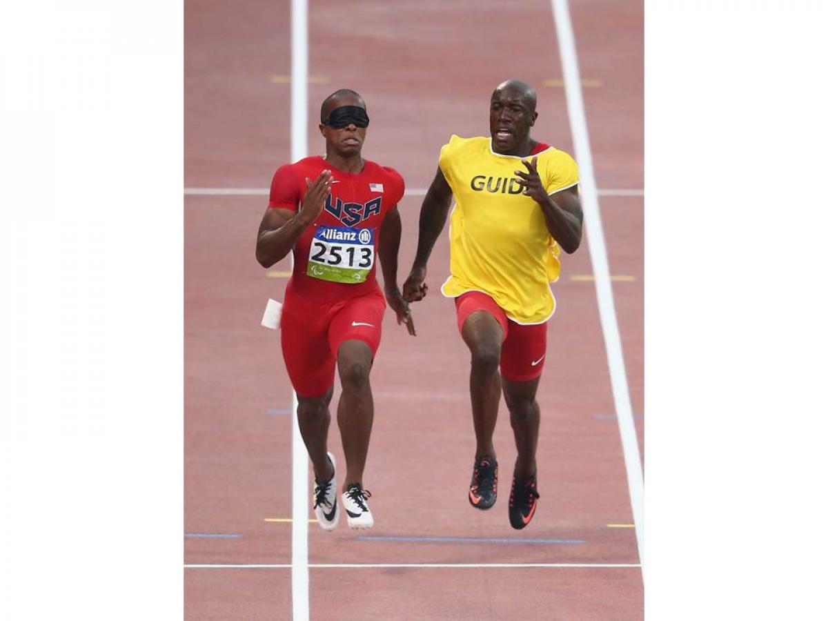 two men running, one with red clothes, one with a yellow t shirt saying guide