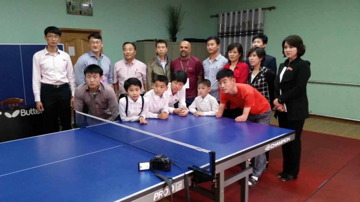 Agitos - North Korea workshops Group picture of kids and adults around a table tennis table