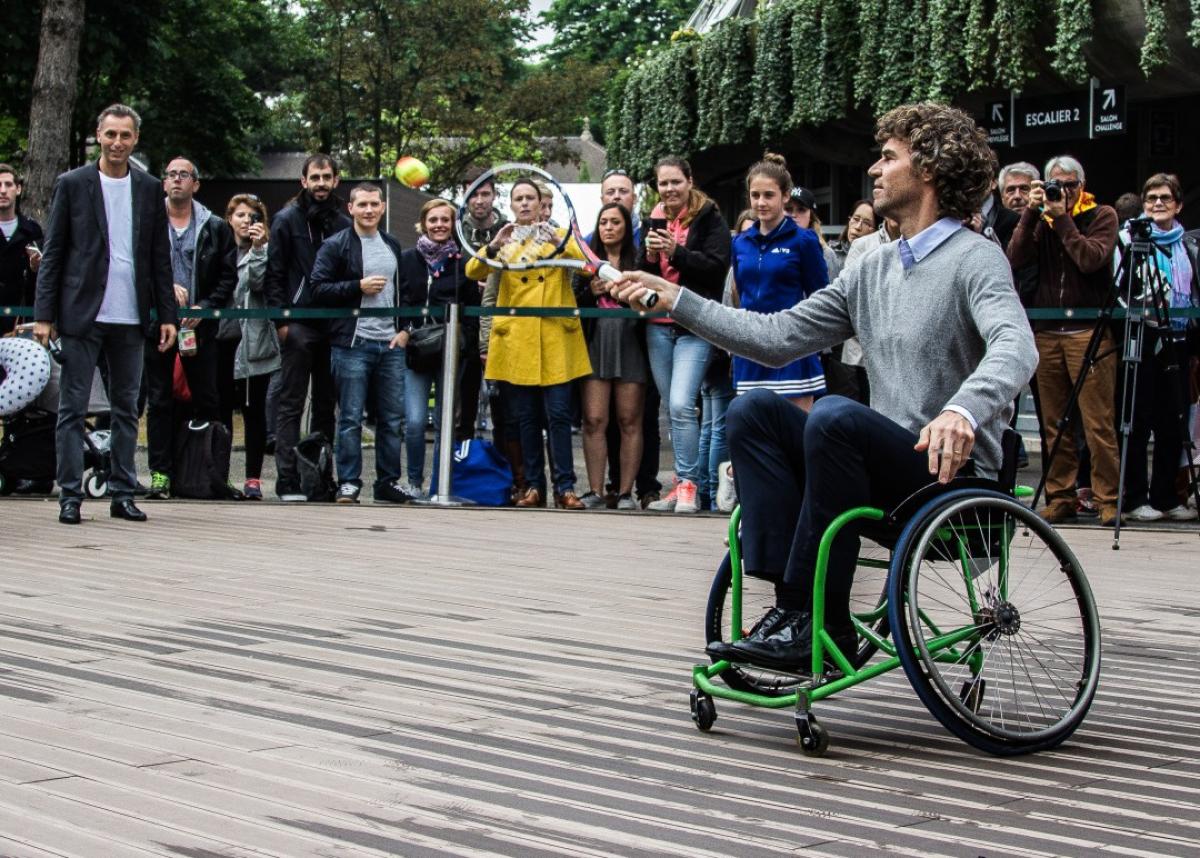 An athlete in a wheelchair hitting a ball with a tennis racket. 