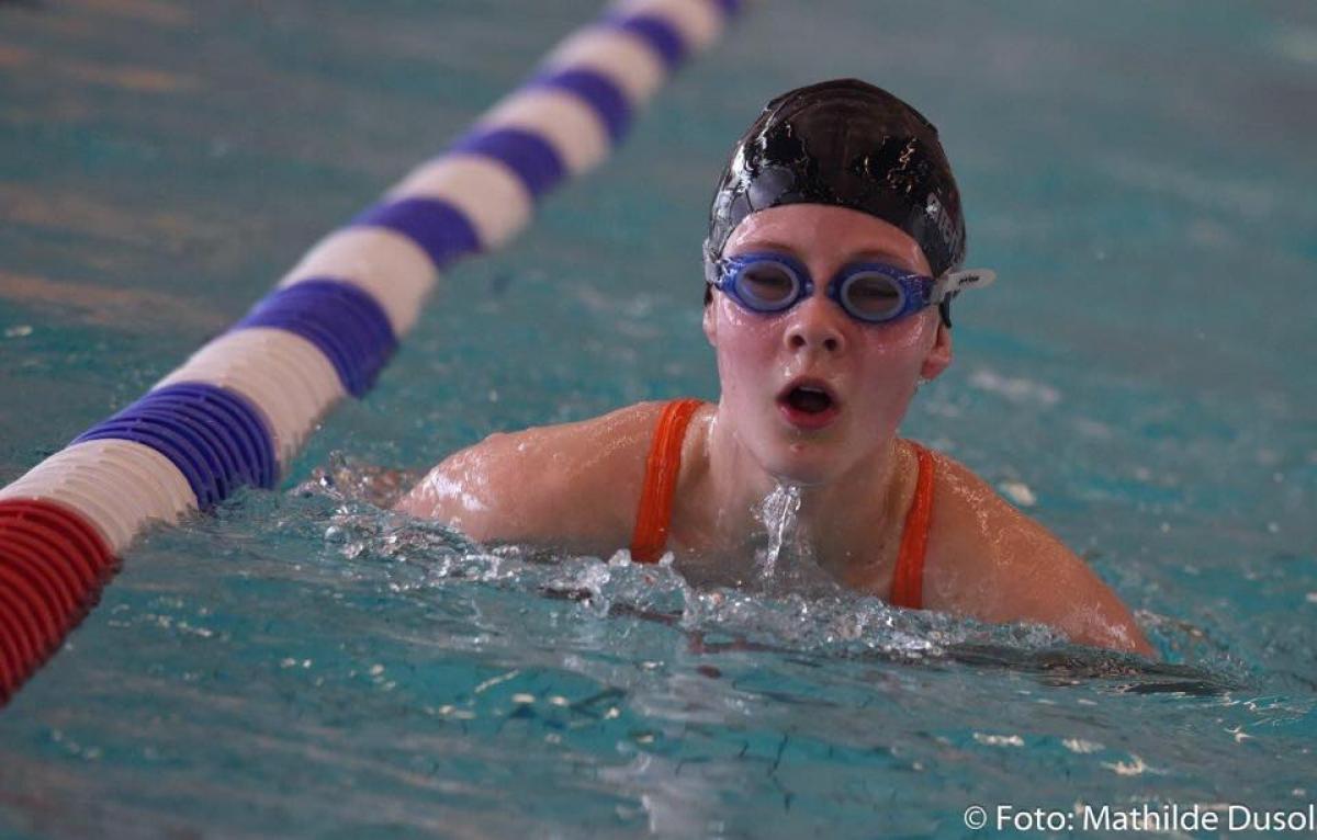 Girl swimming in the pool with swimcap and goggles on. 