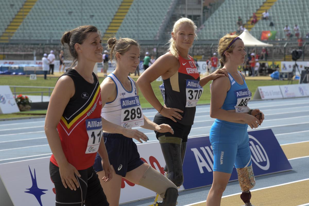 Group of women with leg prosthetics standing in a stadium, one is looking into the camera