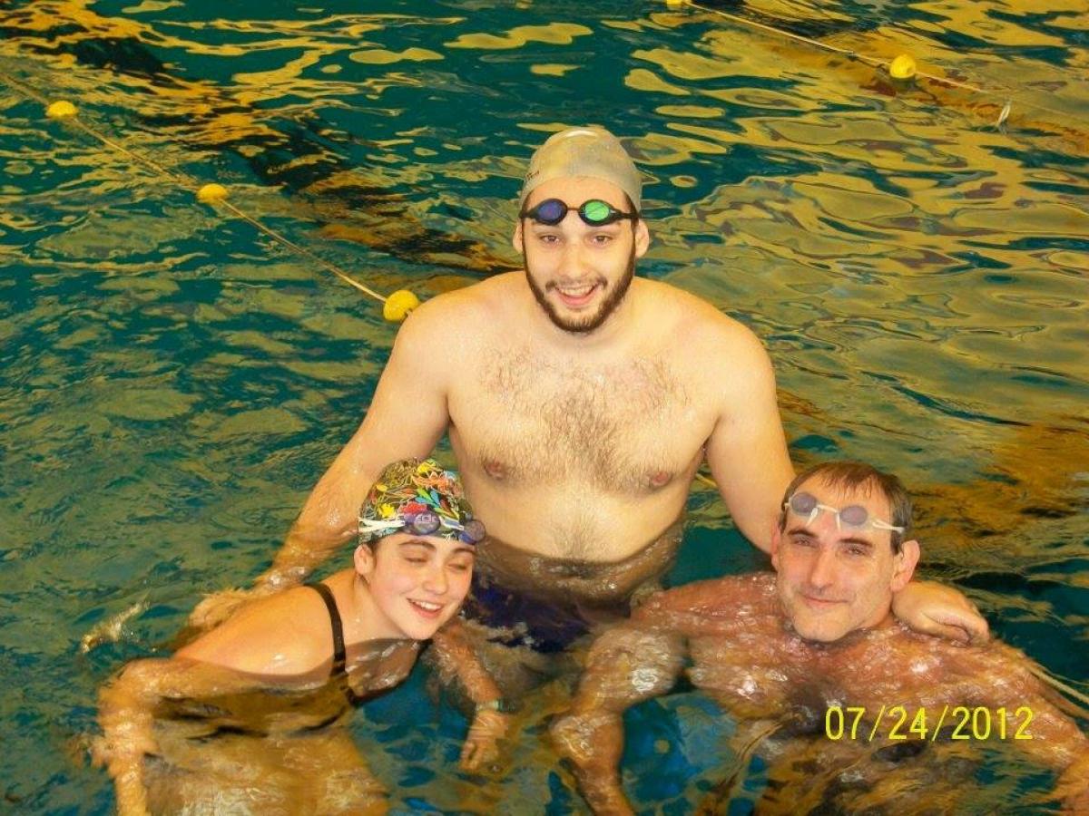 Three people in a pool, smiling to the camera